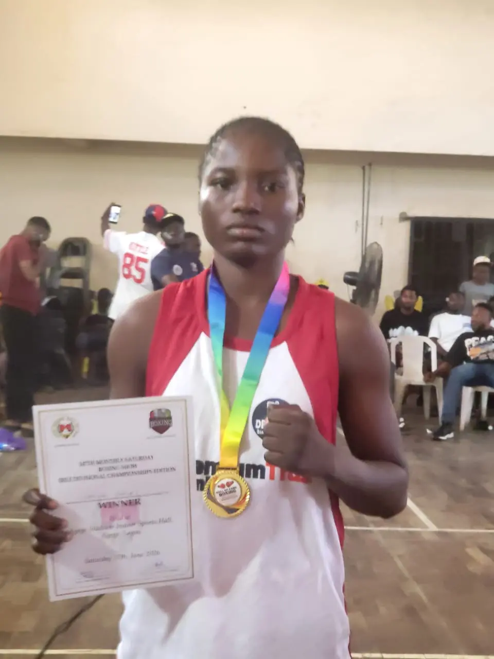 A young boxer holding up her gold medal and winner’s certificate